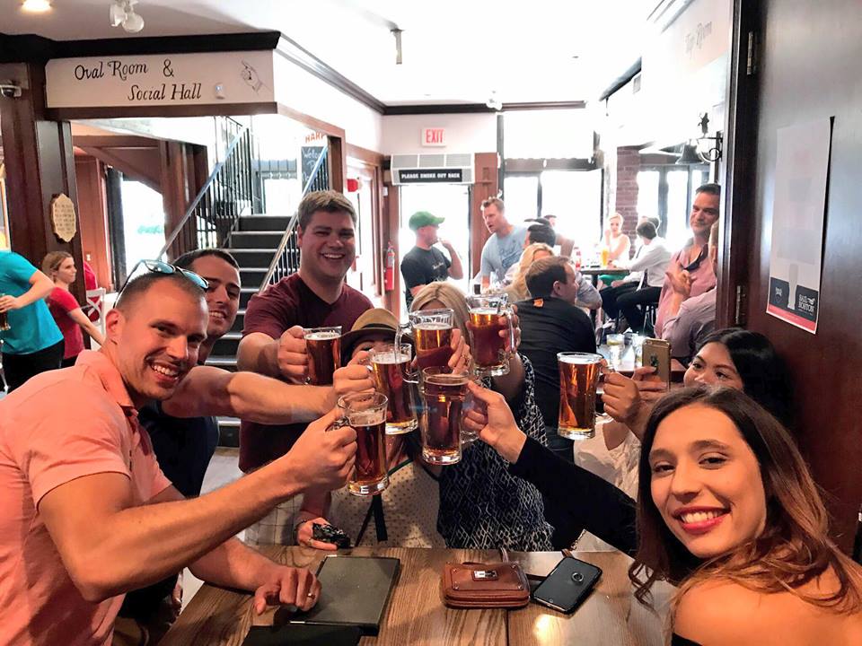 Bell_in_Hand_Cheers a group of people sitting at a table with wine glasses
