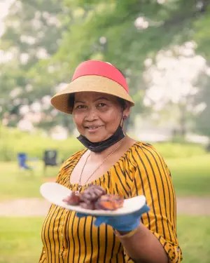 Person in a striped shirt offers a plate of grilled food outdoors.