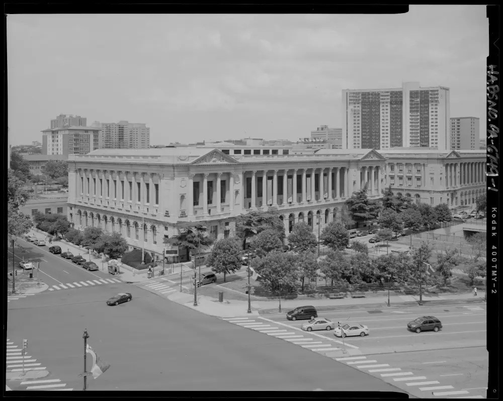 Historic library building with columns, surrounded by trees, and a modern cityscape in the background.