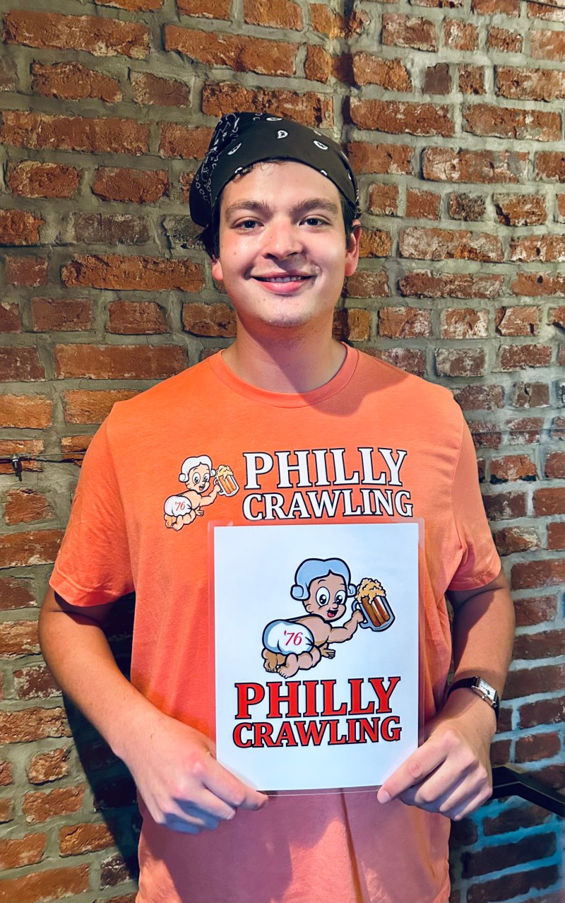 Person in an orange 'Philly Crawling' shirt holding a matching sign against a brick wall.