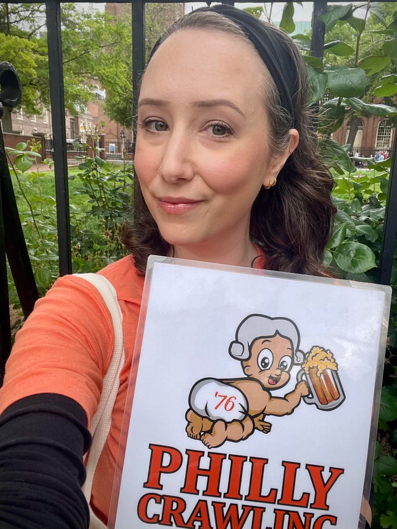 Woman holding 'Philly Crawling' sign, cartoon mascot with beer mug.